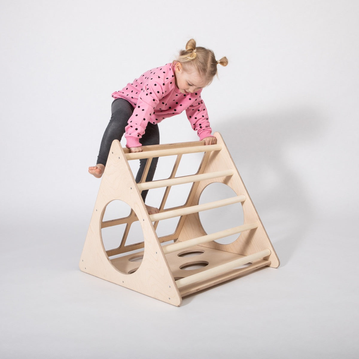 Toddler crawling over wooden climbing triangle with cutout details