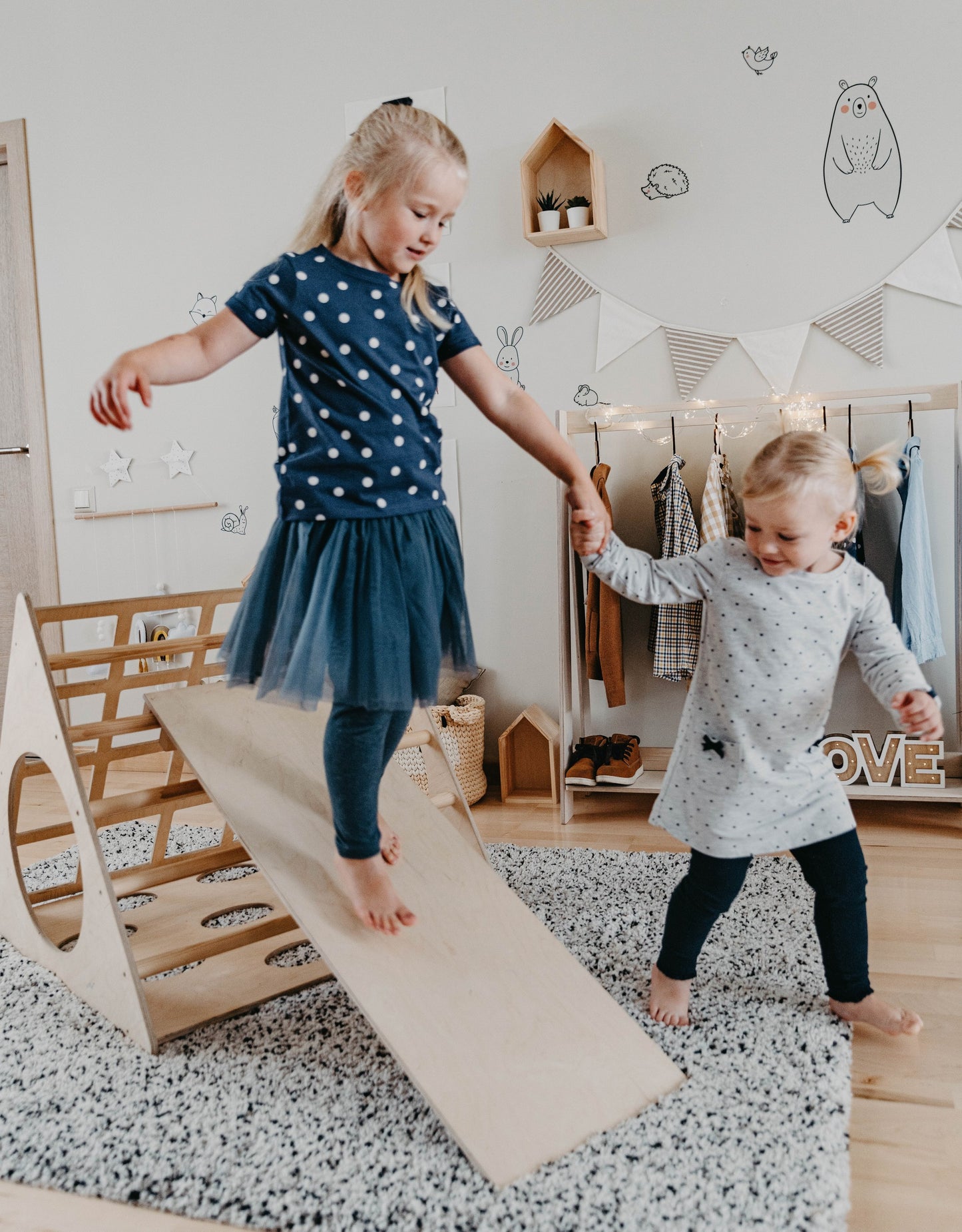 Two young children playing on wooden climbing triangle with ramp, engaging in active gross motor play