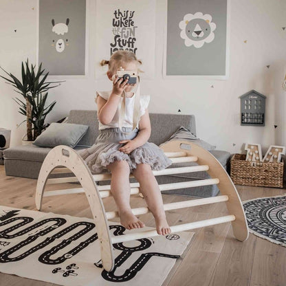 Girl sitting on wooden climbing arch used as rocker in playroom setting