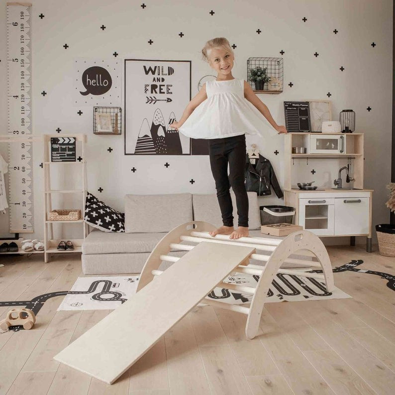 Girl climbing up attached ramp on wooden arch rocker in styled playroom