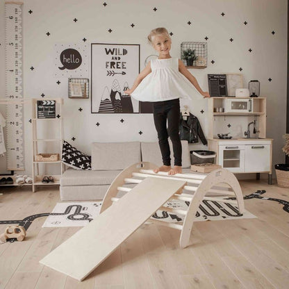 Girl climbing up attached ramp on wooden arch rocker in styled playroom