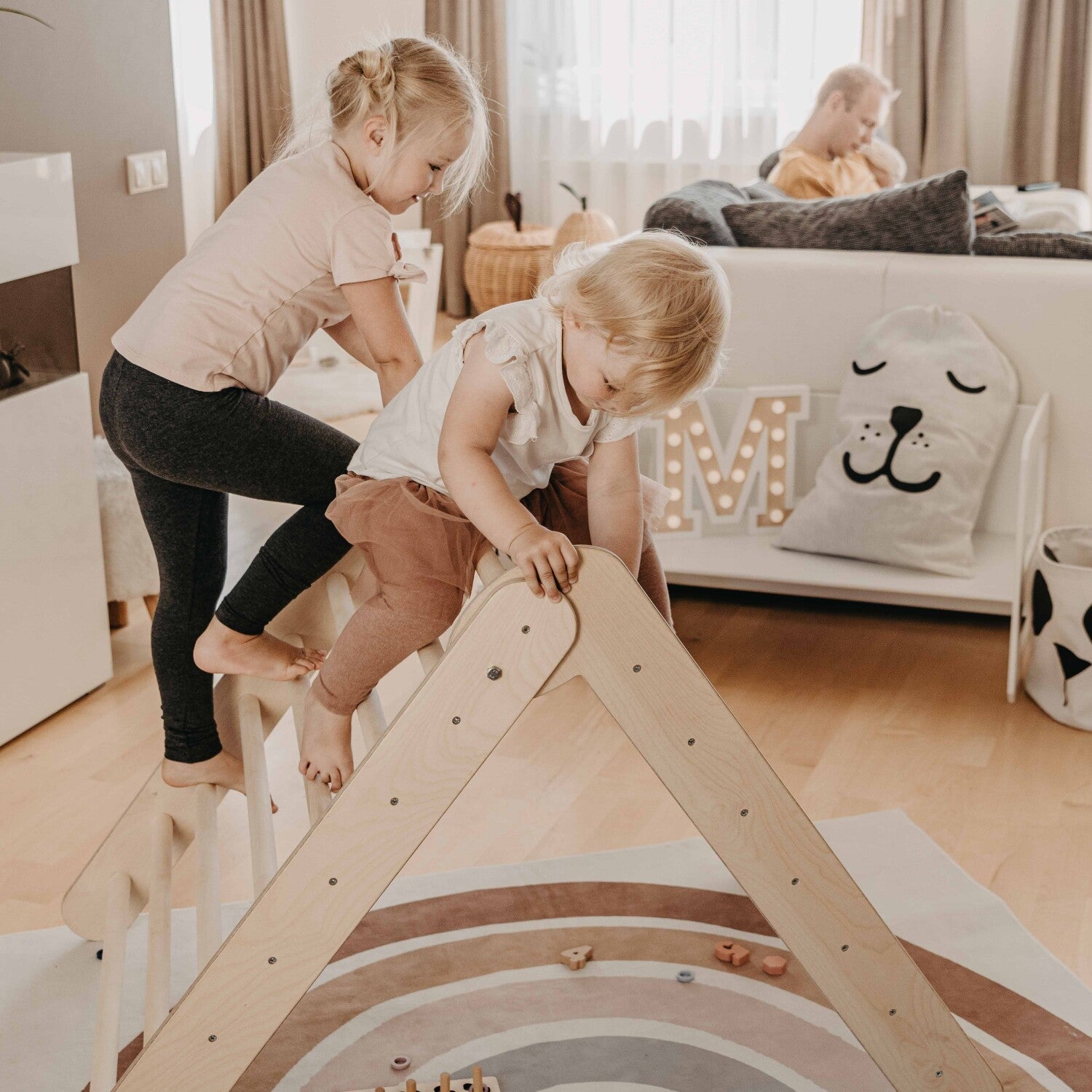 Two toddlers climbing on wooden triangle in bedroom with toys nearby
