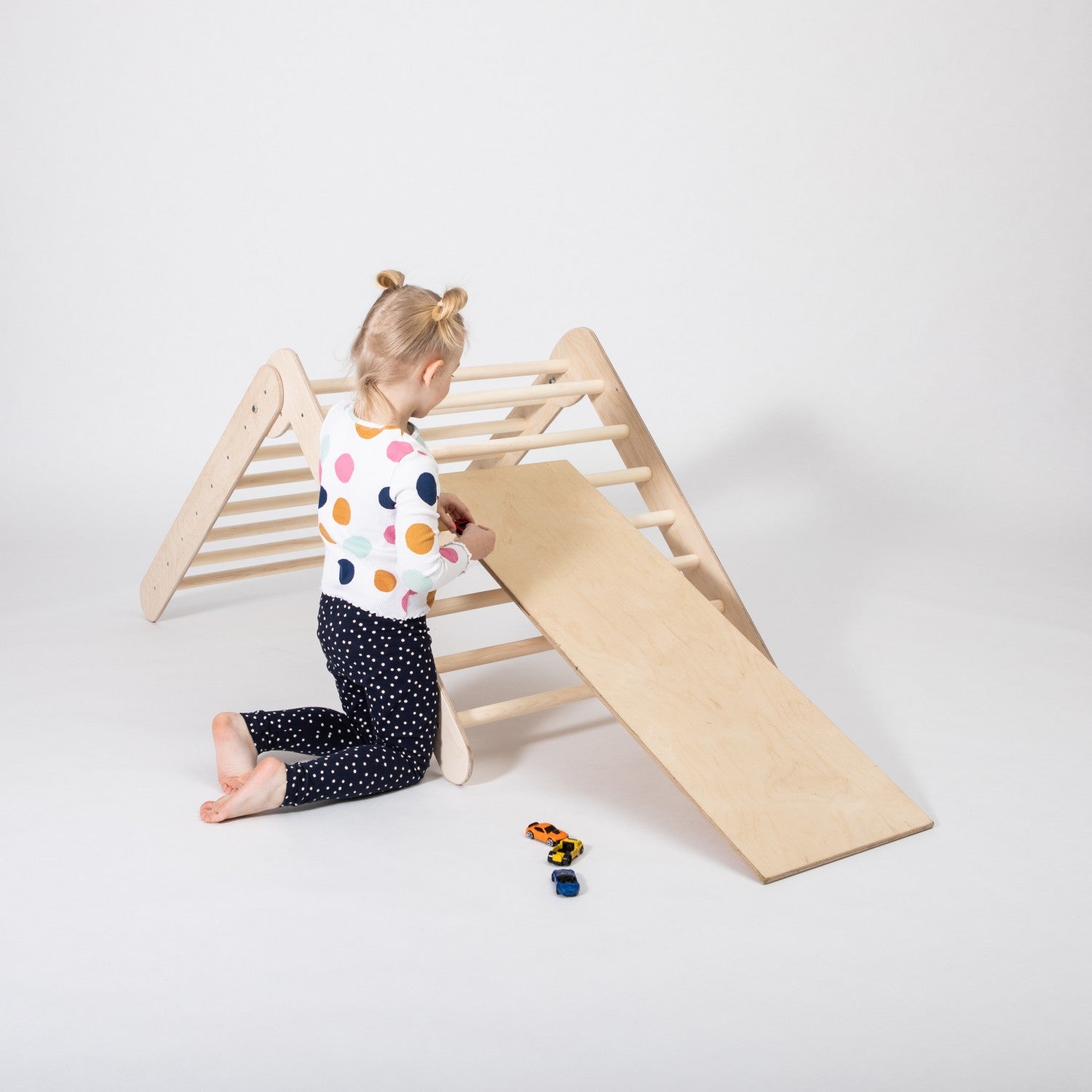 Toddler climbing the wooden triangle and preparing to slide down the ramp