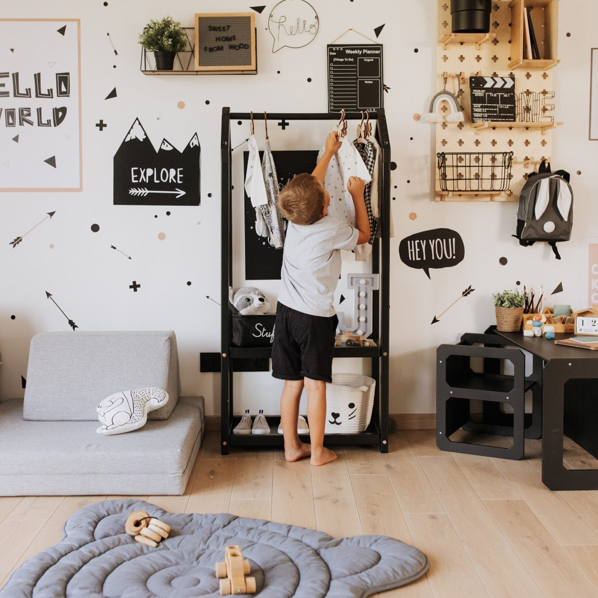 Child reaching for clothes on black house-shaped clothing rack in modern playroom setting