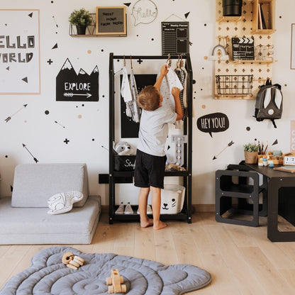 Child reaching for clothes on black house-shaped clothing rack in modern playroom setting