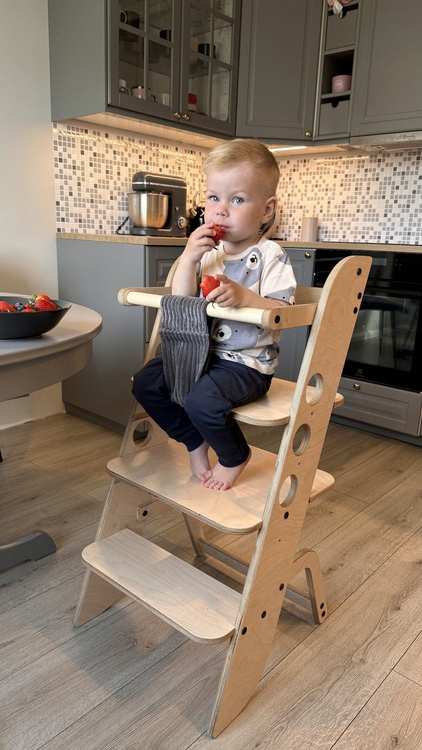 Young child seated in adjustable learning tower high chair at kitchen dining area