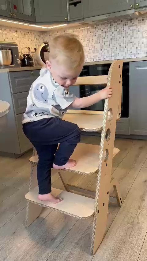 Toddler climbing and reaching on Louis learning tower platform in kitchen setting