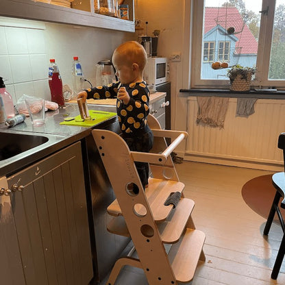 Young child engaging with wooden learning tower as kitchen helper during meal prep