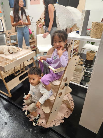 Two young children using learning tower together in playroom setting with Montessori display