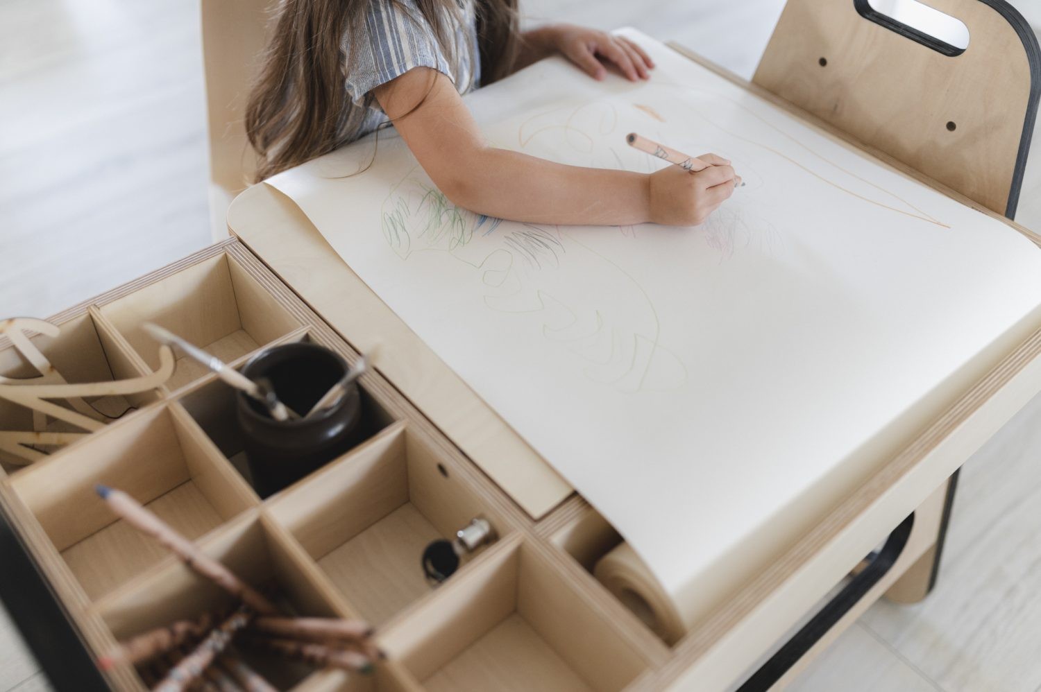 Girl drawing on white work surface with storage compartments visible below