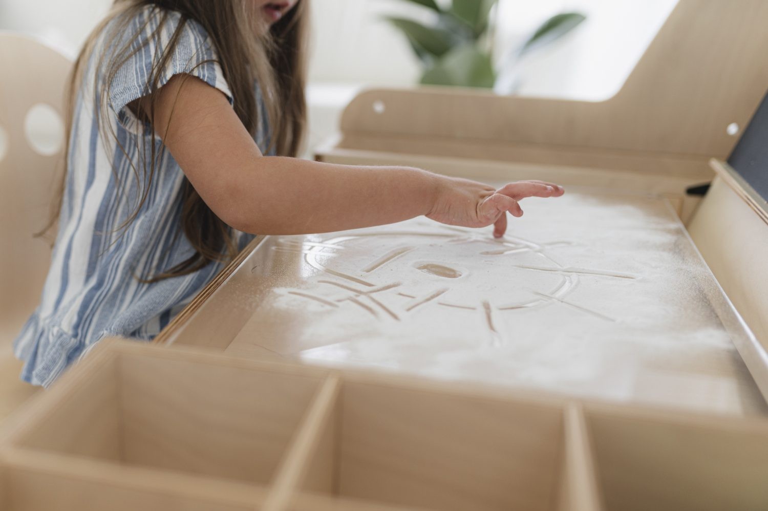 Child's hands exploring sensory sand play in Luula table storage compartment