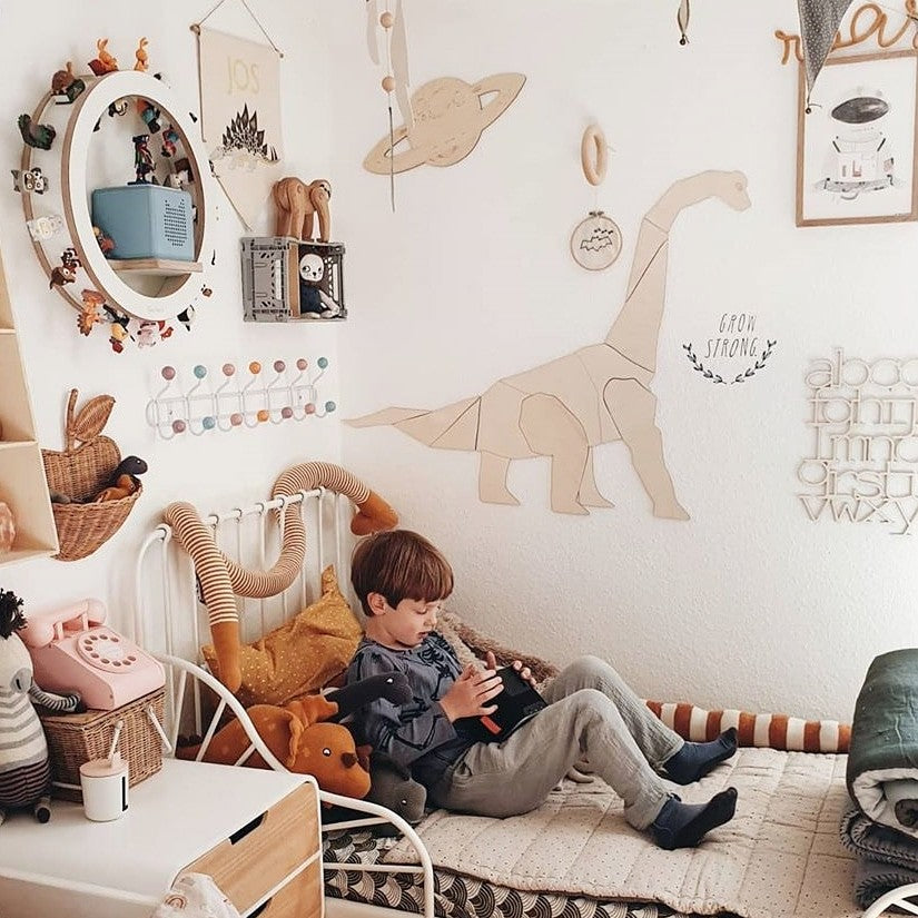 Child sitting against wall with wooden diplodocus wall art and coordinating dinosaur-themed nursery decor