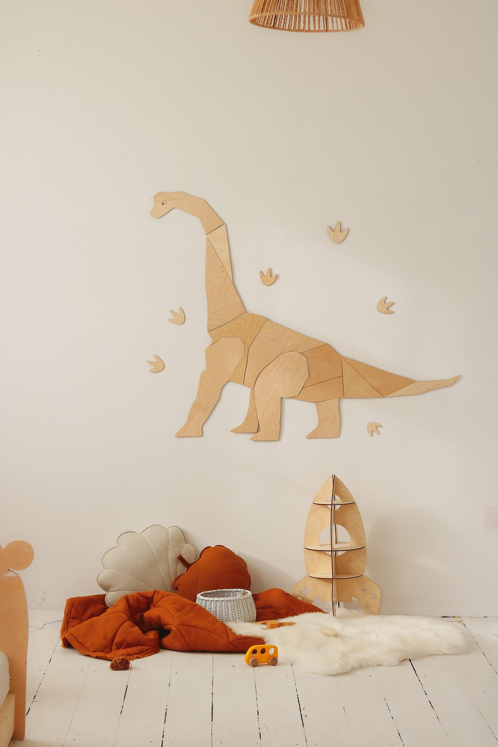 Wooden diplodocus wall piece with geometric footprint details above floor cushions and play area