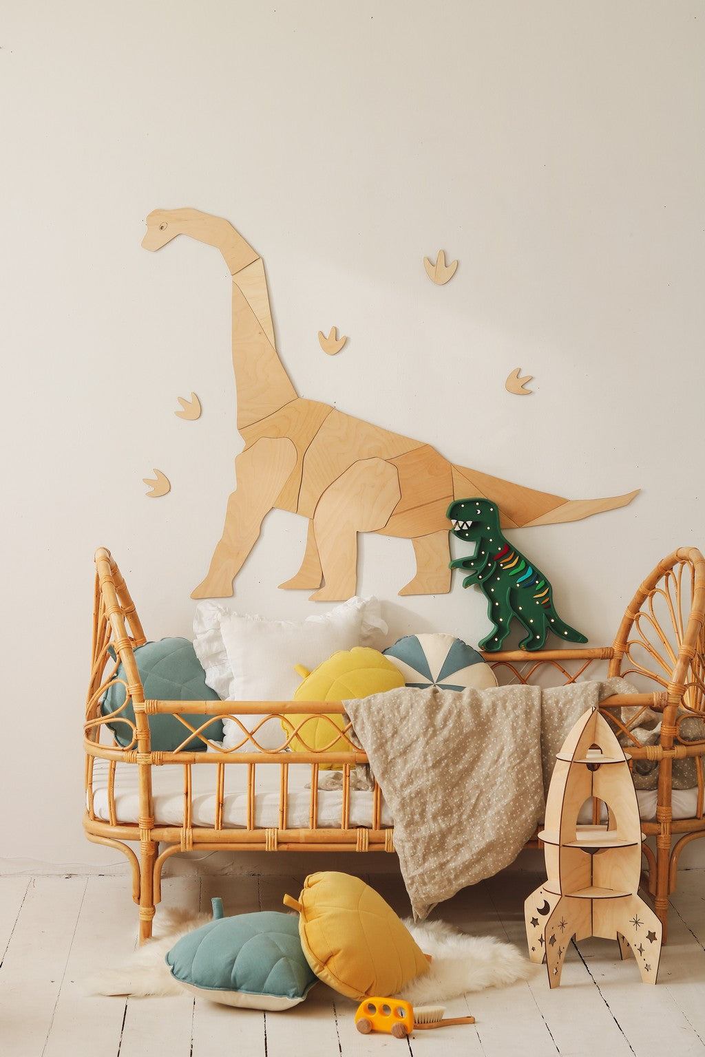 Natural wood diplodocus wall decor mounted above crib with colorful pillows and toys