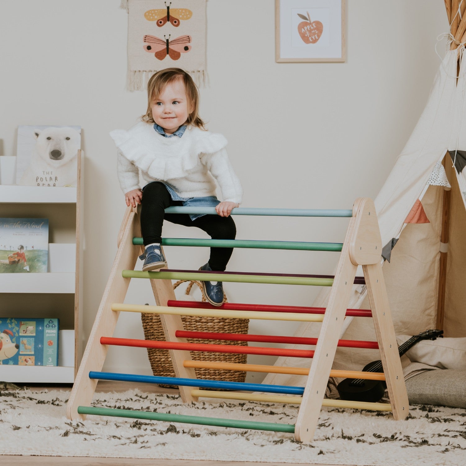 Child practicing climbing skills on rainbow Pikler Triangle with colorful horizontal bars