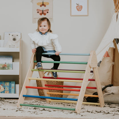 Child practicing climbing skills on rainbow Pikler Triangle with colorful horizontal bars