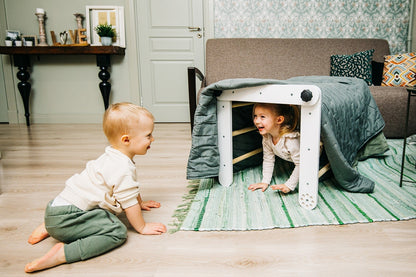 Child crawling under white Pikler triangle tunnel configuration in bedroom setting