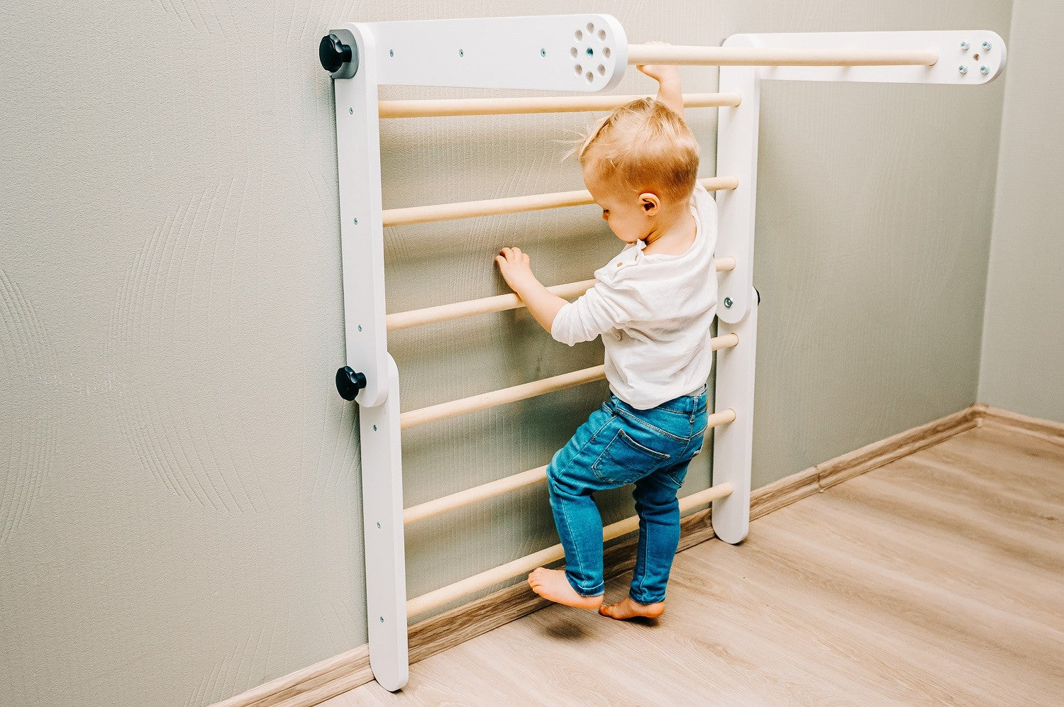 Toddler climbing wooden ladder rungs on vertical Pikler triangle wall configuration