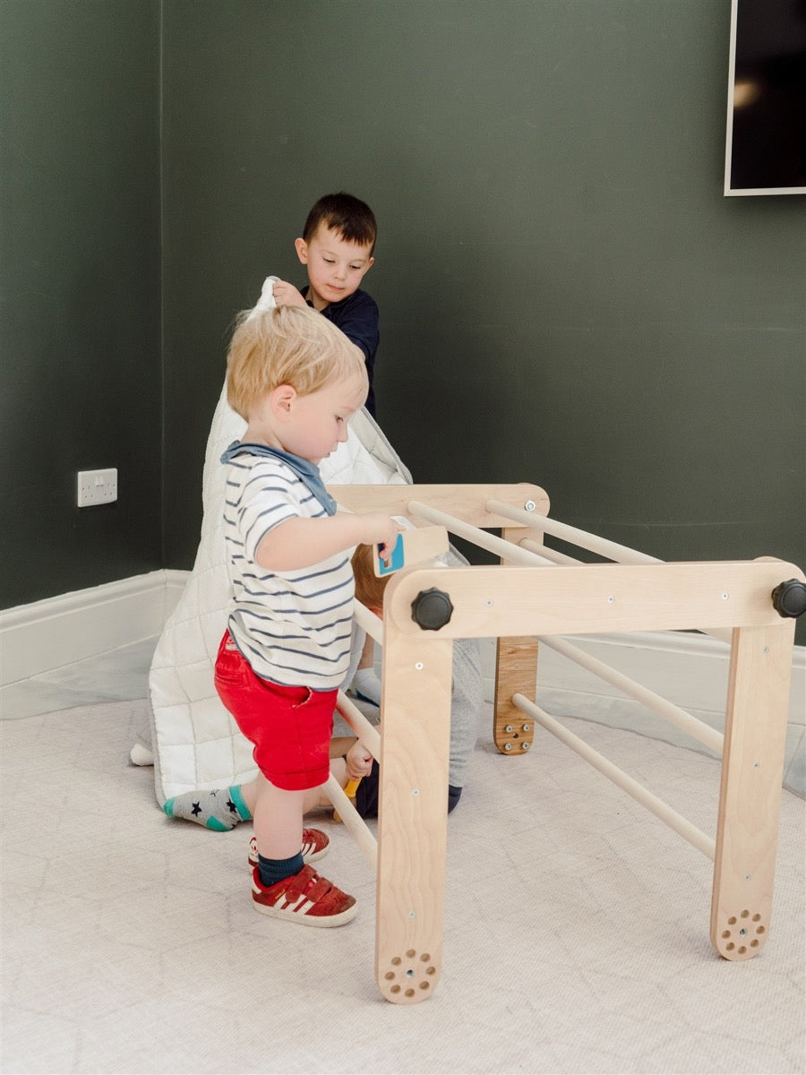 Two children playing on natural birch Pikler triangle in flat position indoors