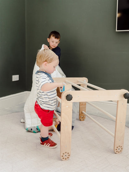 Two children playing on natural birch Pikler triangle in flat position indoors