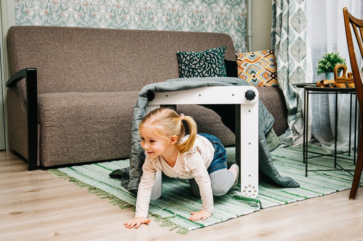 Child crawling through white Pikler triangle tunnel under living room sofa
