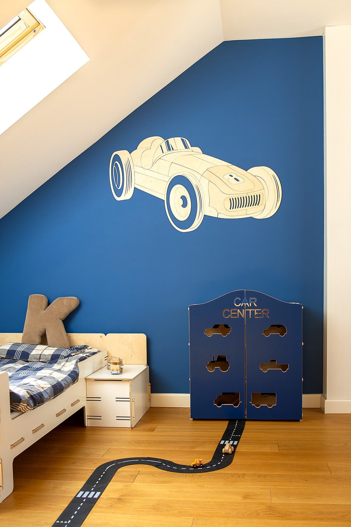 Wooden formula one car decal on blue wall next to white nightstand and toy garage