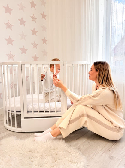 Caregiver interacting with baby in white round crib with star wall decal