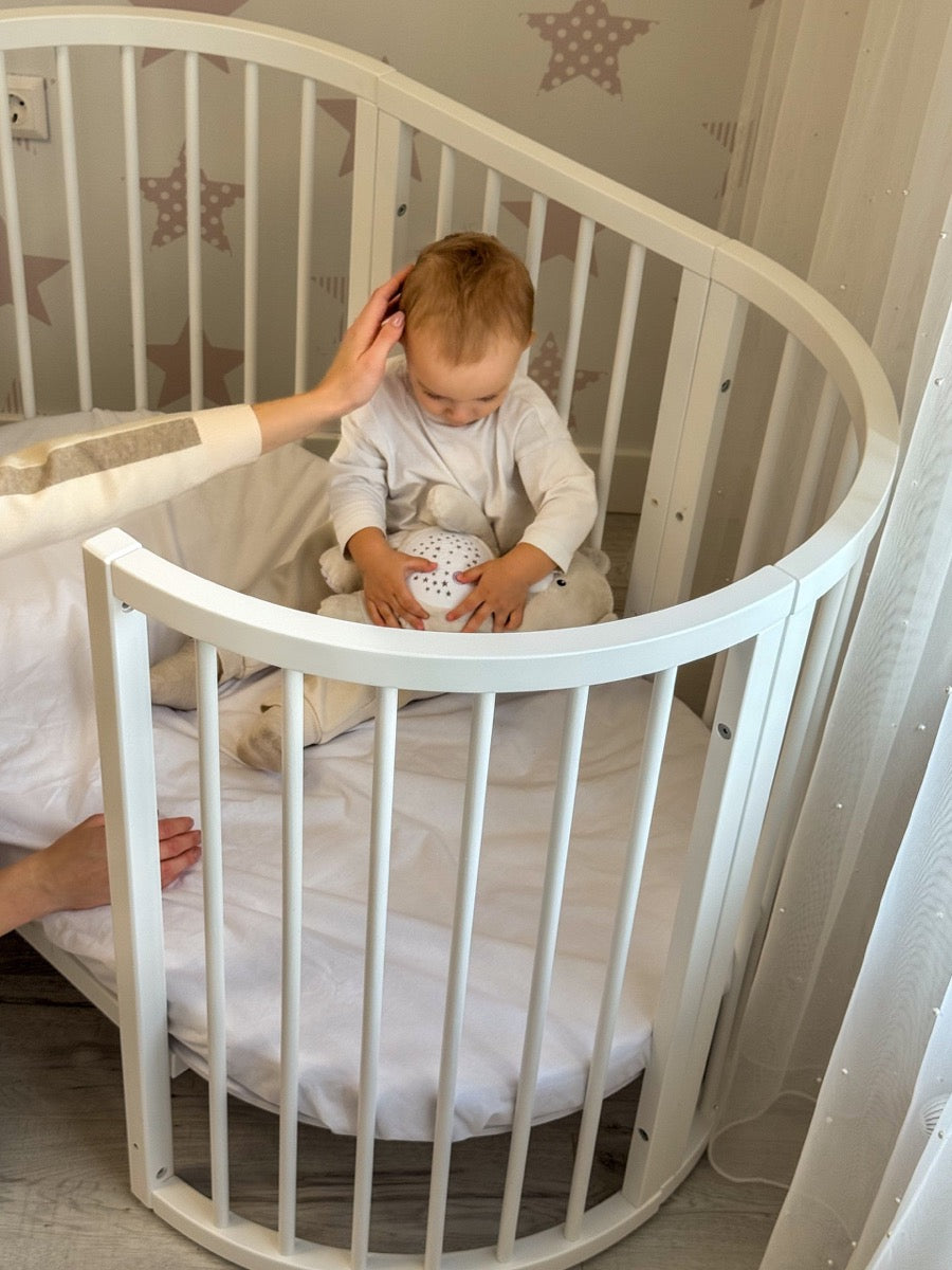Overhead view of happy baby inside round white crib on mattress