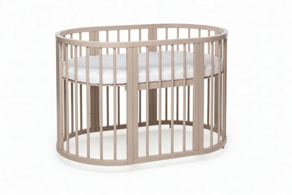Oval OLIN baby crib with removable side panel and adjustable mattress base in natural wood