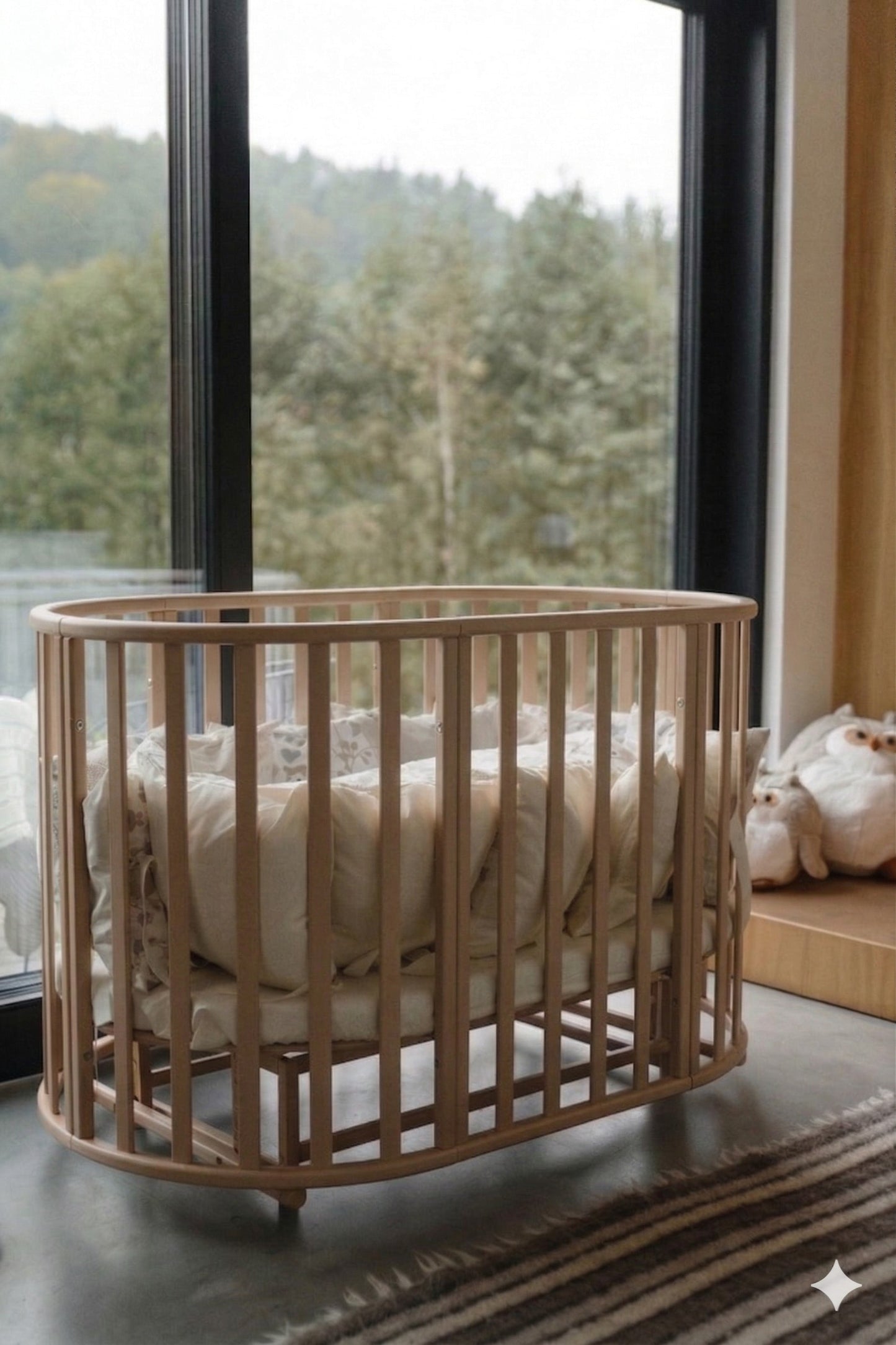 Round beechwood baby crib with mattress by window, styled with cream bedding