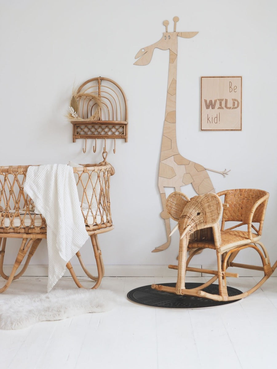 Wooden safari giraffe wall decoration displayed in neutral nursery with wicker furniture and safari-themed decor