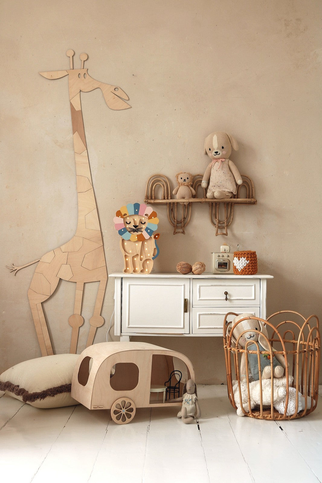 Natural wood giraffe wall decoration beside white dresser with shelves holding toys and nursery accessories