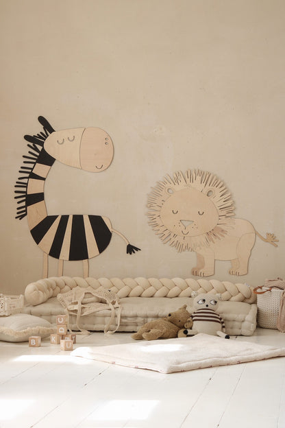 Wooden safari lion and striped zebra wall art displayed above cream floor cushion