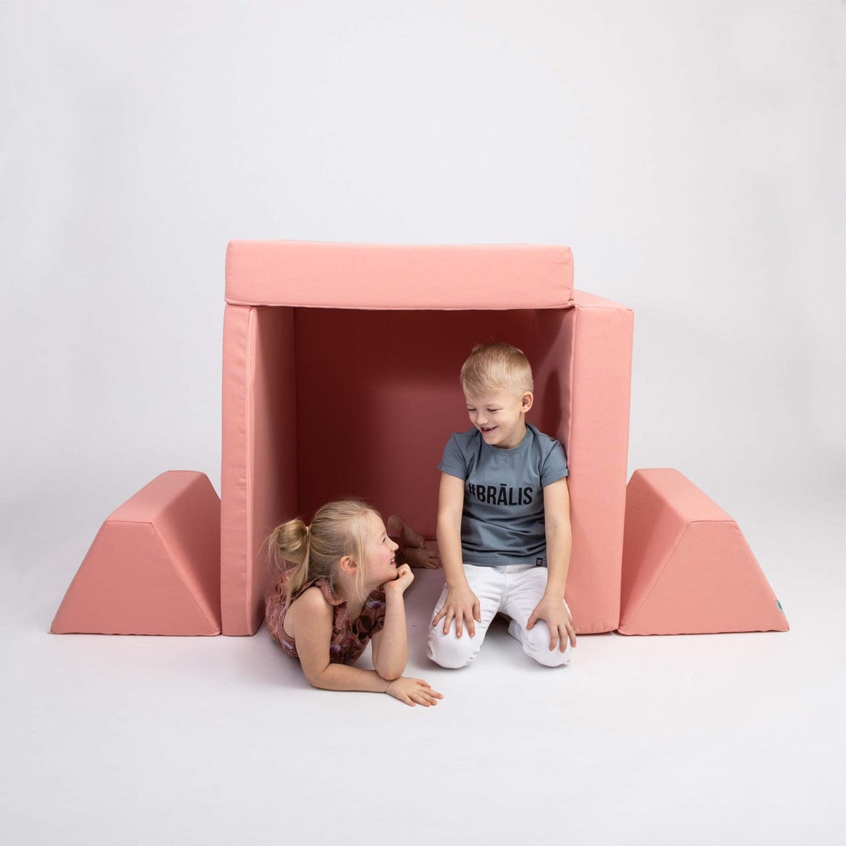 Two children playing inside a salmon pink foam play tent made from activity mattress pieces