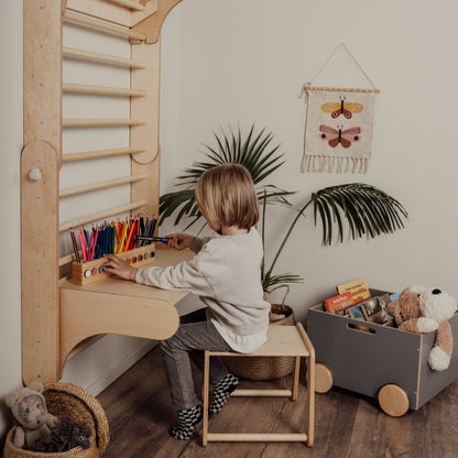 Child drawing at wooden desk attached to Swedish wall with storage shelf