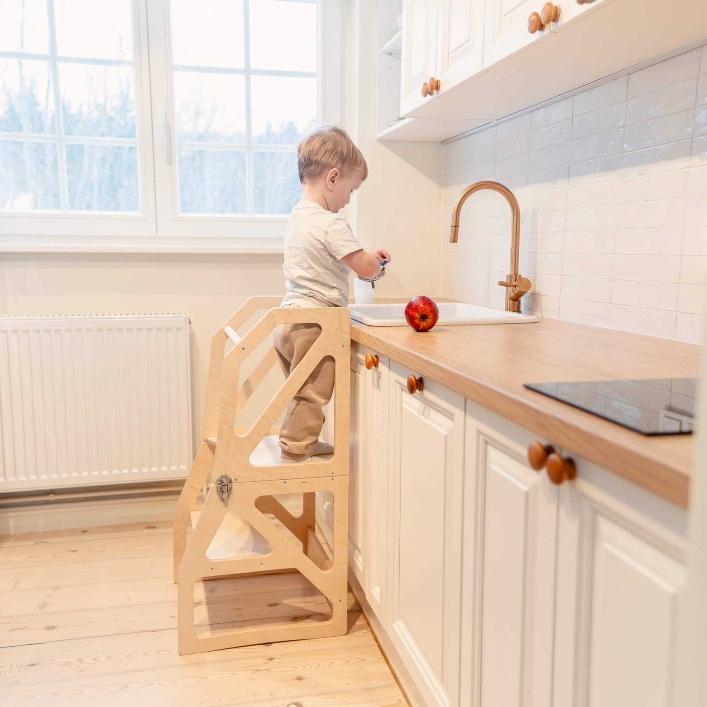 Child standing on natural wood kitchen tower stepping stool at kitchen counter