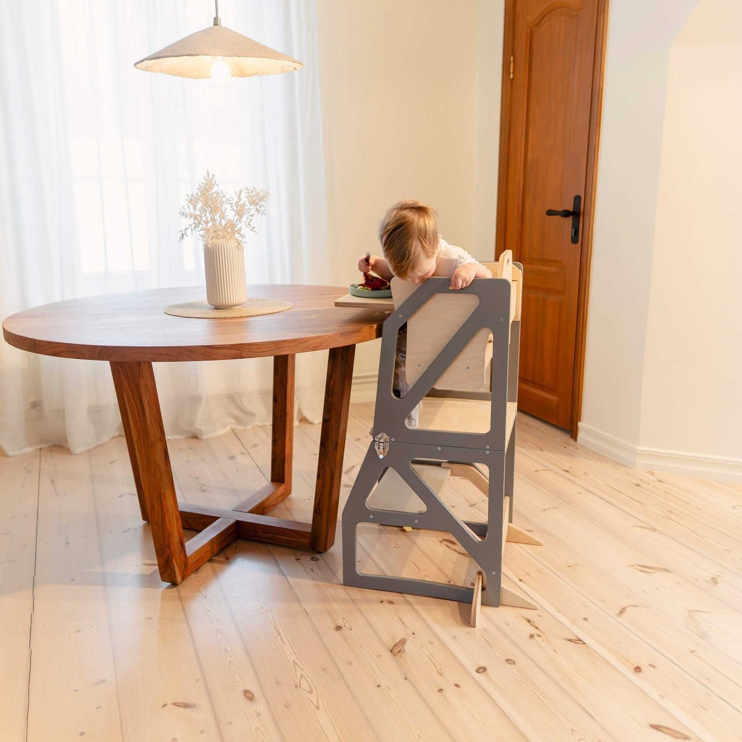 Child seated at round wooden table using gray Modustep chair in living room