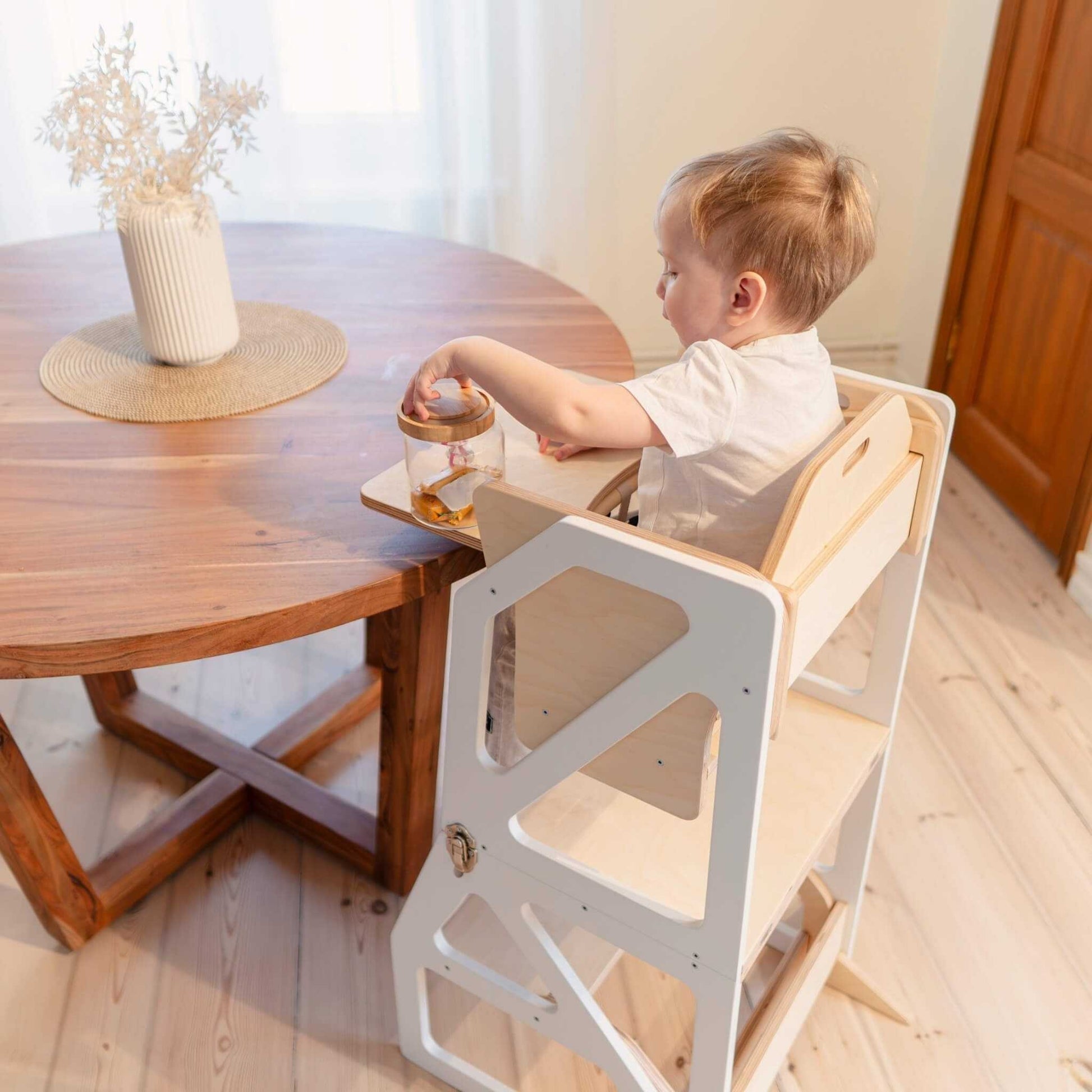 Toddler sitting at dining table on natural wood Modustep high chair with tray
