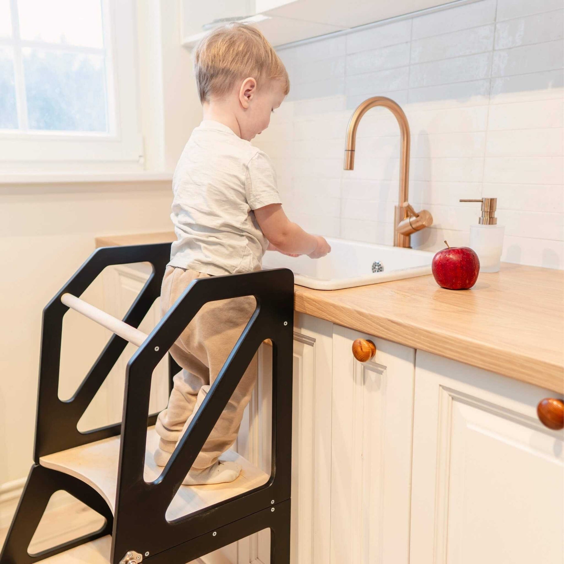 Young child washing hands at kitchen sink using black Modustep step tower