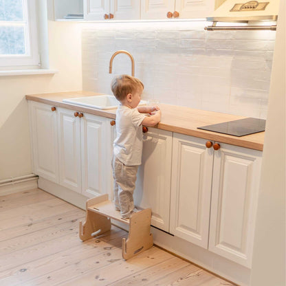 Young child reaching kitchen countertop with natural wood kitchen tower step