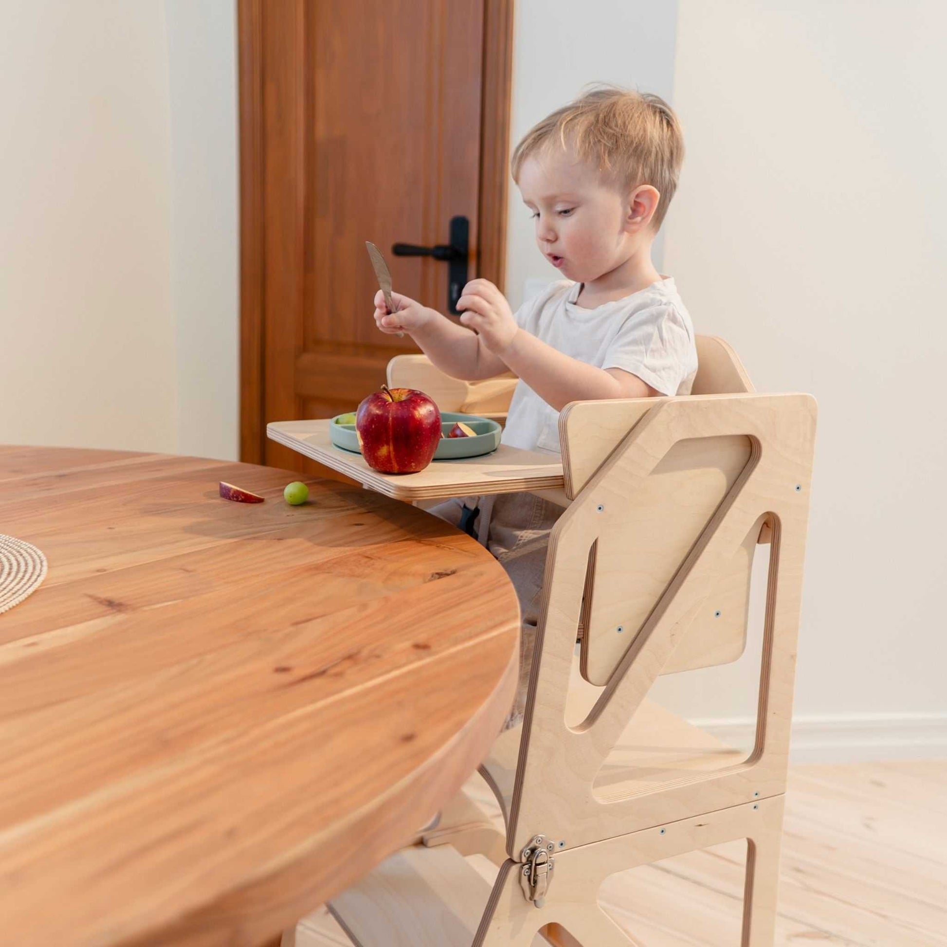 Toddler in Modustep high chair at wooden dining table eating snack