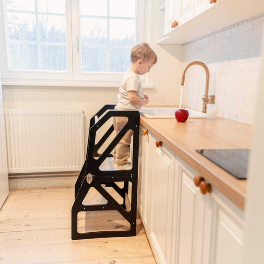 Toddler standing on black kitchen tower at adult countertop, reaching toward sink