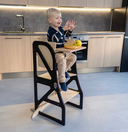 Toddler eating fruit at attached tray table on black kitchen learning tower