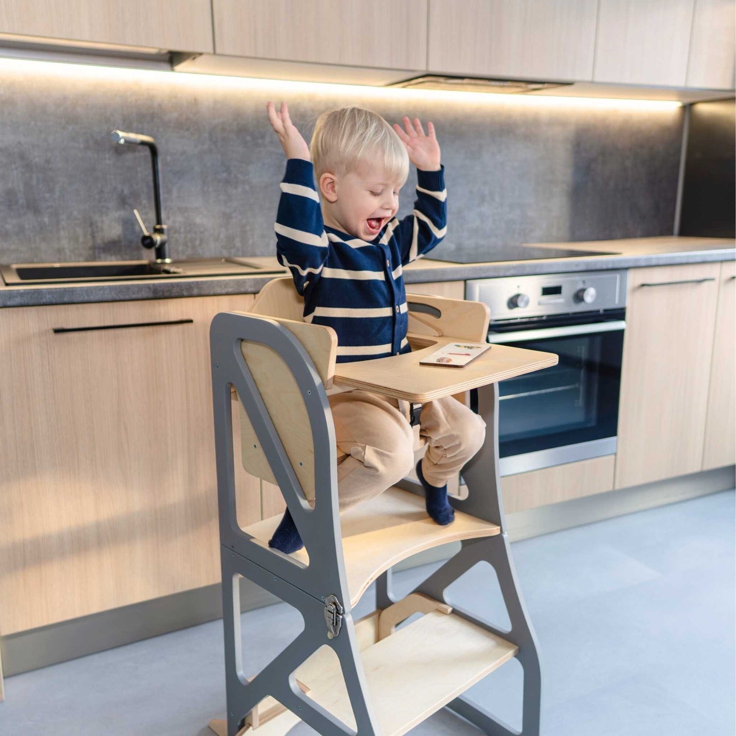 Toddler at kitchen tower table reaching and playing during mealtime