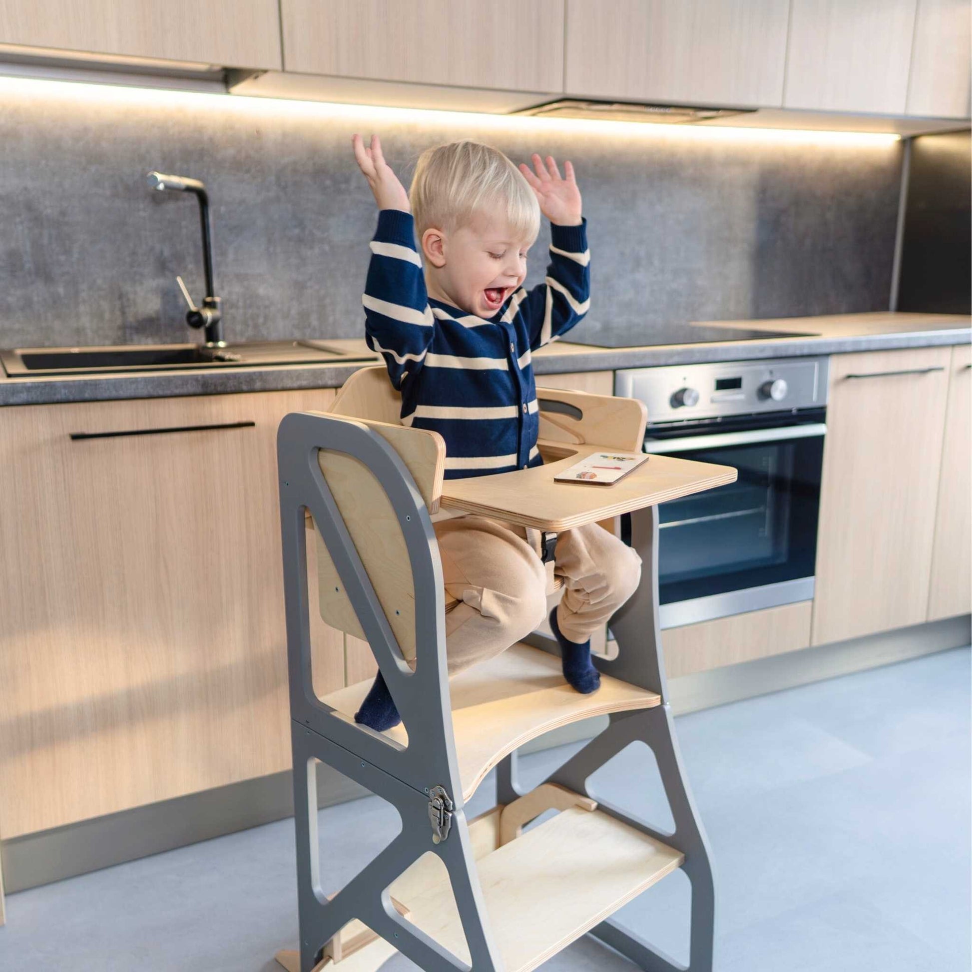 Toddler at kitchen tower table reaching and playing during mealtime