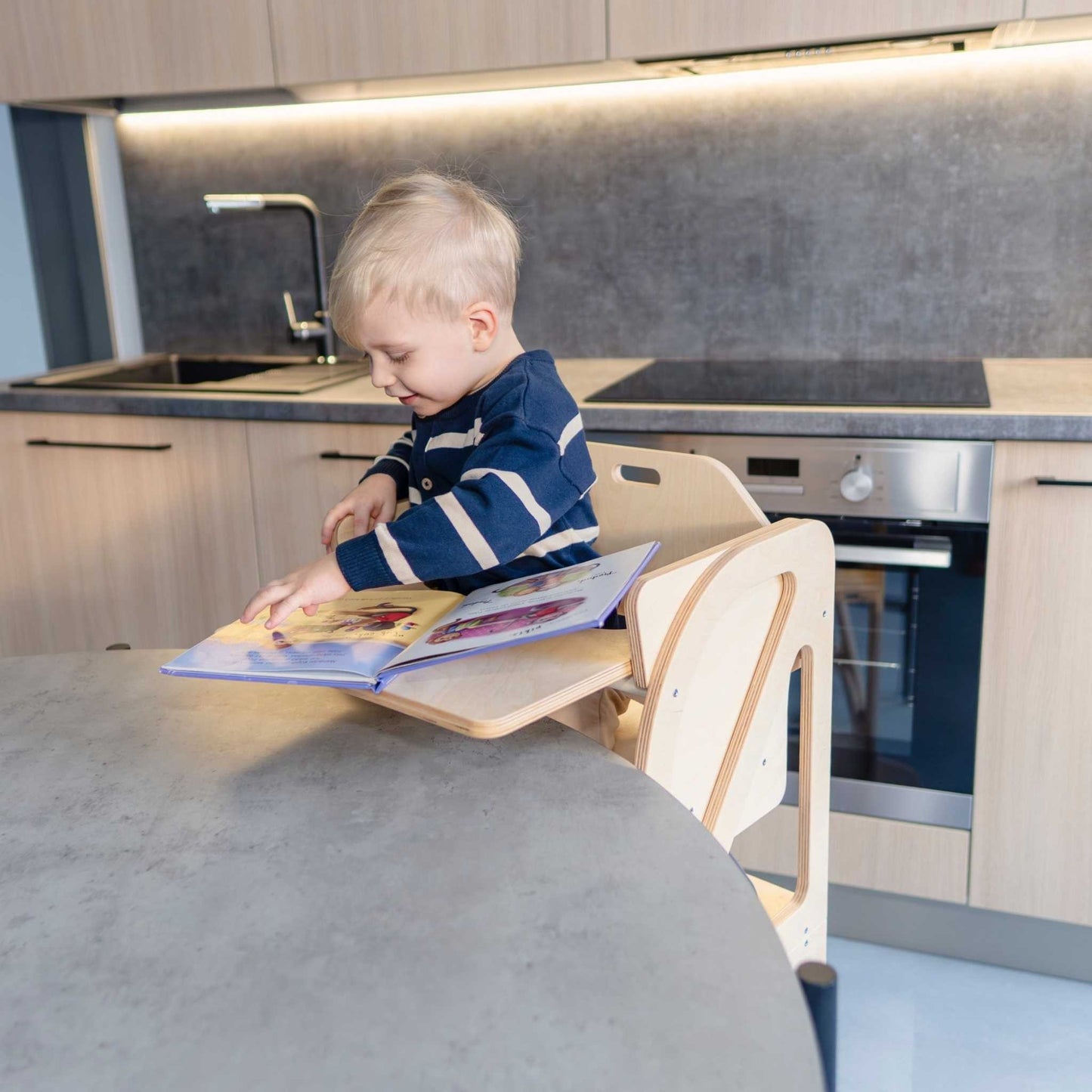 Child reading at birch plywood table attached to kitchen tower learning step