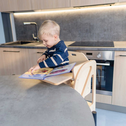 Child reading at birch plywood table attached to kitchen tower learning step