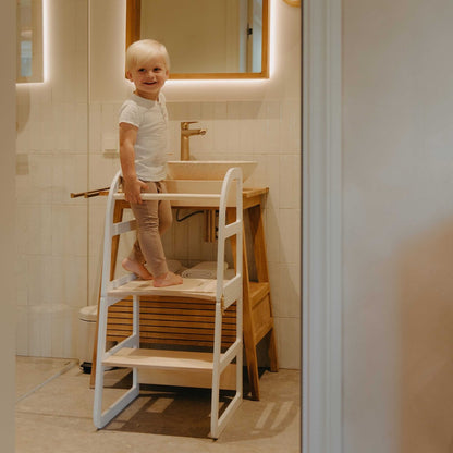 Toddler standing in natural wood kitchen tower at bathroom sink