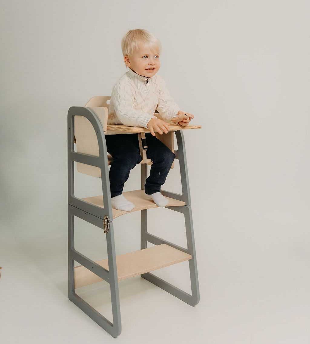 Child reaching toy on top of natural kitchen tower demonstrating height