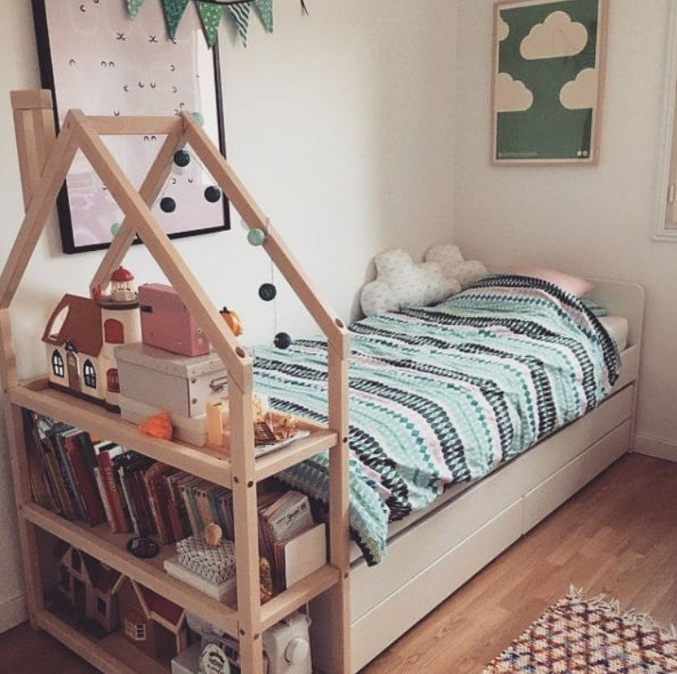 Natural wood house shelf next to bed storing books and toys in Montessori bedroom
